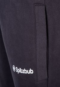 Dunkelgraue Jogginghose mit weichem Material, ausgestattet mit einer Seitentasche und weißem "Spitzbub"-Logo am linken Bein. Schlichtes Design und Passform.
