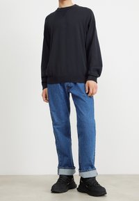 Schwarz übergroßer Sweatshirt mit gerippten Bündchen und Halsausschnitt, kombiniert mit hellblauen Denim-Jeans mit umgeschlagenen Säumen und schwarzen Sneakern.