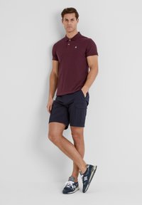 Maroon polo shirt, navy cargo shorts, blue sneakers. Casual outfit with a solid design and contrasting colors, featuring buttons on the collar.