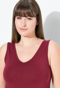 Haut sans manches bordeaux avec un décolleté en V profond. Texture lisse avec une coupe ajustée, peu de détails au niveau du col.