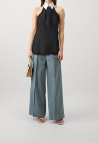 Black halter top with a white collar, paired with wide-leg light blue denim trousers and beige handbag. Platform sandals complete the look.