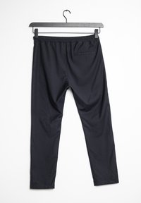 Svarta byxor med elastisk midja, slät struktur, slim fit och en bakficka. Hänger på en svart metallgalge mot en vit bakgrund.
