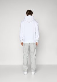 Witte hoodie met een grote capuchon, gecombineerd met lichtgrijze joggingbroek. Het materiaal lijkt zacht, met een relaxte pasvorm en geribde manchetten.
