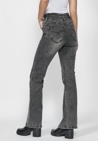 Jeans negros acampanados con un acabado desgastado, cuentan con dos bolsillos traseros con costura curvada, usados con botas de plataforma negras.
