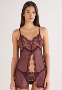 Lace babydoll in deep plum with sheer polka dot fabric, adjustable straps, front button detail, and scalloped edges. Includes matching panty.