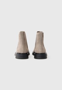 Bottines en daim gris avec une semelle en caoutchouc noir lisse, comportant des panneaux élastiques sur les côtés et un logo discret au niveau du talon.