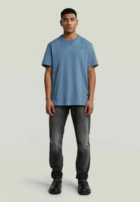 Jasnoniebieska bawełniana koszulka z okrągłym dekoltem, krótkimi rękawami i małym detalem logo, zestawiona z ciemnoszarymi dżinsami i czarnymi butami.