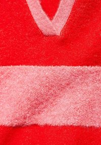 Close-up van zacht, pluizig rood en roze stof met een roze V-vormige brei-detail aan de bovenkant.