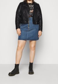 Veste en cuir noir de motard, t-shirt graphique, mini-jupe en denim bleu et bottes noires à lacets. Comprend des fermetures éclair et des couleurs contrastées.