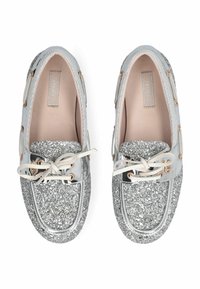 Chaussures bateau en paillettes argentées avec un bout en cuir verni brillant, intérieur beige, accents en lacets et œillets dorés.