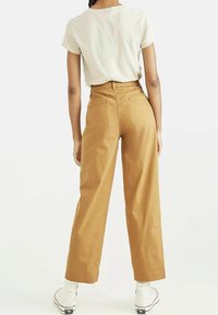 Högmidjade, vida byxor i tanfärgad bomull, med bakfickor och stickade detaljer, tillsammans med vita sneakers.