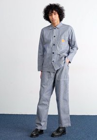Blue and white striped shirt with a collar and buttons, paired with matching striped pants. Model wears black shoes.