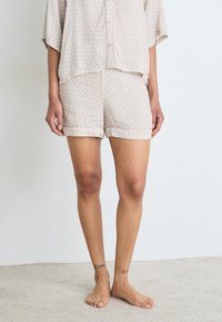 Kortärmad, ljus beige pyjamasset med ett enkelt geometriskt mönster; lös passform på toppen och shortsen med uppvikta fållar. Mjuk tyg.