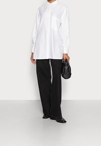 Chemise blanche à boutons avec une poche poitrine unique, associée à un pantalon large noir et un petit sac à main matelassé noir.