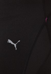 Černá sportovní látka s lesklým logem Puma. Textura je hladká s viditelnými švy a malým růžovým prošíváním.