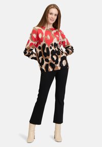 Knit sweater in tan with bold red, black, and leopard print; paired with black pants and beige heeled boots. Relaxed fit, long sleeves.