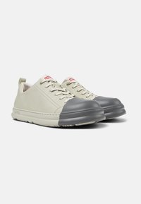 Sneaker in pelle grigia chiara con puntale in gomma grigia, lacci piatti e suola texturizzata. Etichetta logo rossa sulla linguetta; design minimalista senza motivi.