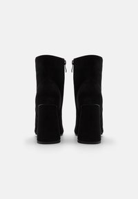 Bottines en suède noir avec un haut talon carré et un détail de fermeture éclair à l'arrière. Texture lisse, design structuré et bout arrondi.