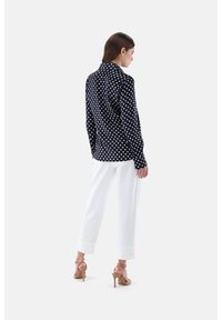 Navy polka dot blouse with long sleeves, buttoned collar, worn with white trousers and nude high-heeled sandals. Simple, clean design.
