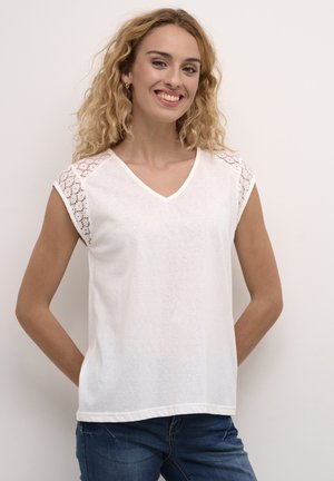 White V-neck t-shirt made of lightweight fabric, featuring lace accents on the shoulders. Worn with denim jeans.