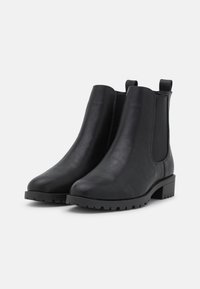 Botas de tobillo de cuero negro con paneles laterales elásticos, puntera redondeada y un tacón bajo tipo bloque. Presentan una suela de goma con patrón para mejorar la tracción.