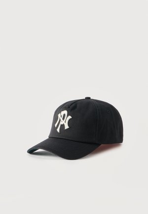 Casquette de baseball noire à visière courbée avec un logo stylisé blanc sur le devant, posée sur un fond blanc uni.