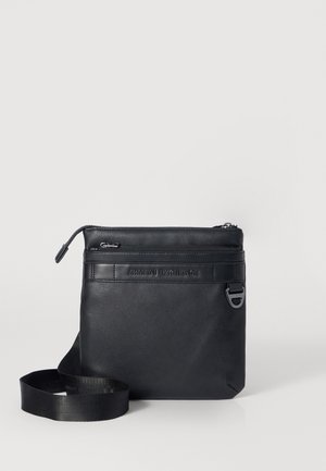Bolso cruzado de piel negra con cierre de cremallera, correa ajustable y logo en relieve "Armani Exchange". Textura suave y forma rectangular.