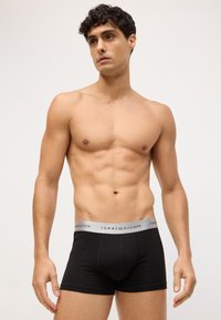 Boxers negros con una cinturilla gris que presenta el texto "TOMMY HILFIGER". Hechos de material suave, con forma ajustada que acentúa el torso.