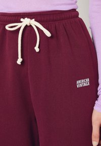 Burgundijas kokvilnas sporta bikses ar baltu auklu un sānu kabatu. Priekšpusē ir neliels balts "American Vintage" logo. Mīksta tekstūra.