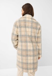 Uldfrakke med et stort ternet mønster i beige, brun og grå nuancer; har en spids krave og lange ærmer, mid-længde design.