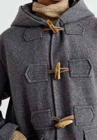 Grå uldfrakke med hætte, der har træknaplukning og påsatte lommer. Tekstureret stof med en struktureret form. Lysebrune detaljer.