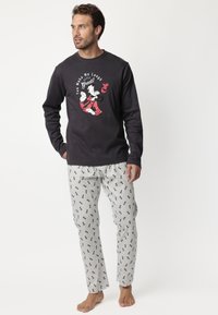 Camisa de pijama negra de manga larga con estampado gráfico; pantalones de pijama grises con un patrón de dibujos animados repetido; tejido suave, corte relajado.
