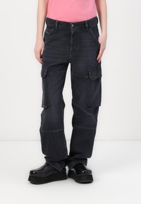 Pantalones cargo de mezclilla oscura con un corte holgado, múltiples bolsillos laterales y detalles de costura en contraste. Combinados con zapatos de plataforma negros y robustos.
