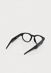 Schwarze Brille mit geometrischem Design, ausgestattet mit scharfen, eckigen Gläsern und schlanken Bügeln. Strukturierte Oberfläche mit metallischen Hardware-Details.