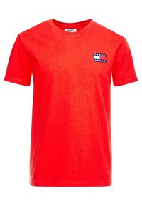 Červené bavlněné tričko s kulatým výstřihem. Má malou námořnickou modrou a bílou nášivku "TOMMY JEANS" na levé straně hrudi. Hladká textura.