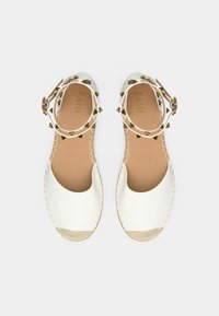 Weiße Espadrilles mit offenem Zehenbereich, Obermaterial aus Leder, beigem Boden, gestreiftem Knöchel mit Nieten und genähten Details entlang der Ränder.