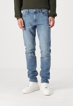 Jeans de mezclilla azul claro con corte ajustado, diseño de cinco bolsillos y un desvanecimiento sutil. Combinados con zapatillas blancas.