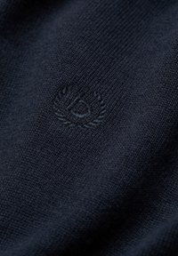 Dunkelblaues gestricktes Gewebe mit einem dezent gestickten Logo, das ein Kreis- und Lorbeerkranzdesign in passendem Garn zeigt.
