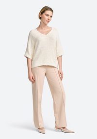 Cremfarbener Pullover mit V-Ausschnitt und weiten Ärmeln, kombiniert mit hellbeigen, maßgeschneiderten Hosen und nudefarbenen, hohen Pantoletten. Einfaches, klares Design.