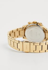 Guld rustfrit stålværk med en linkrem, et rundt urkasse og kronografknapper. Har en poleret overflade og en mærkemærke.