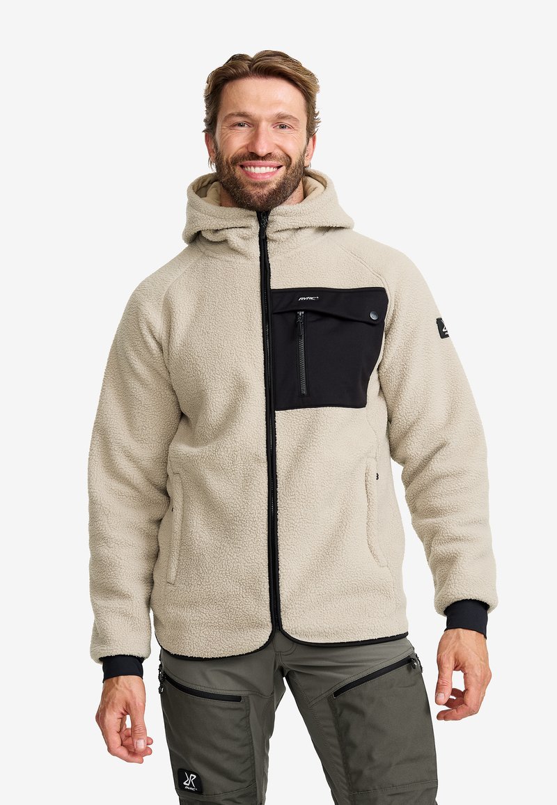 Beige fleecejacka med en svart framficka, blixtlås stängning och justerbar huva. Har texturerat tyg och ribbade muddar.