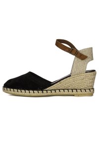 Espadrilles de lona negra con cuña, tira de tela beige en el tobillo y detalle de yute trenzado alrededor de la suela. Cierre con hebilla ajustable.