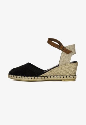 Espadrilles de lona negra con cuña, tira de tela beige en el tobillo y detalle de yute trenzado alrededor de la suela. Cierre con hebilla ajustable.