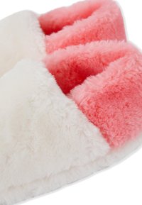 Pantofole morbide e fluffy con esterno bianco e interno foderato di rosa, progettate per il comfort e il calore indoor.