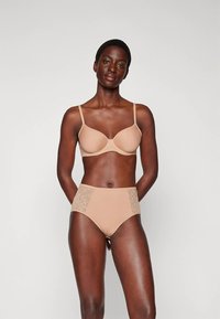 Béžová podprsenka s tenkými ramínky a hladkým povrchem, doplněná béžovými vysokými kalhotkami s krajkovými detaily po stranách.
