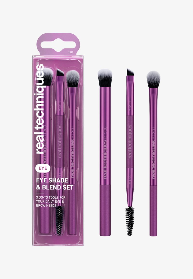 Trois pinceaux de maquillage pour les yeux violets avec des poils noirs et blancs et un pinceau spoolie, présentés à l'intérieur et à l'extérieur d'un emballage transparent.