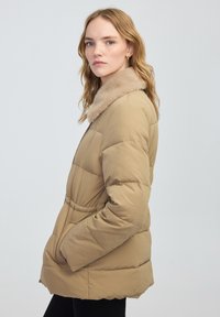 Beżowa kurtka puchowa z kołnierzem z sztucznego futra, pikowany wzór, ściągnięta w pasie i kieszeniami po bokach. Gładki, lekko błyszczący materiał.