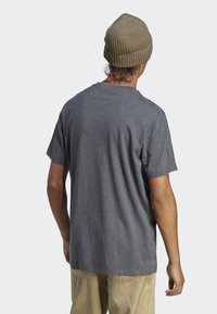 Siva kratka majica s kratkimi rokavi, sproščenega kroja, z okroglih ovratnikom in rebrastim ovratnikom, v kombinaciji z strukturirano olivno zeleni kapo.