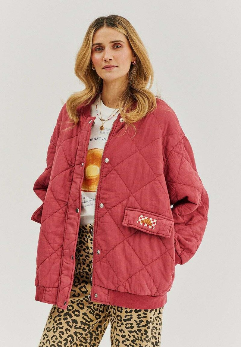 Prešívaná červená bunda so zapínaním na cvoky a náprsníkom, skombinovaná s grafickým tričkom a nohavicami s leopardím vzorom. Textúrovaná látka.