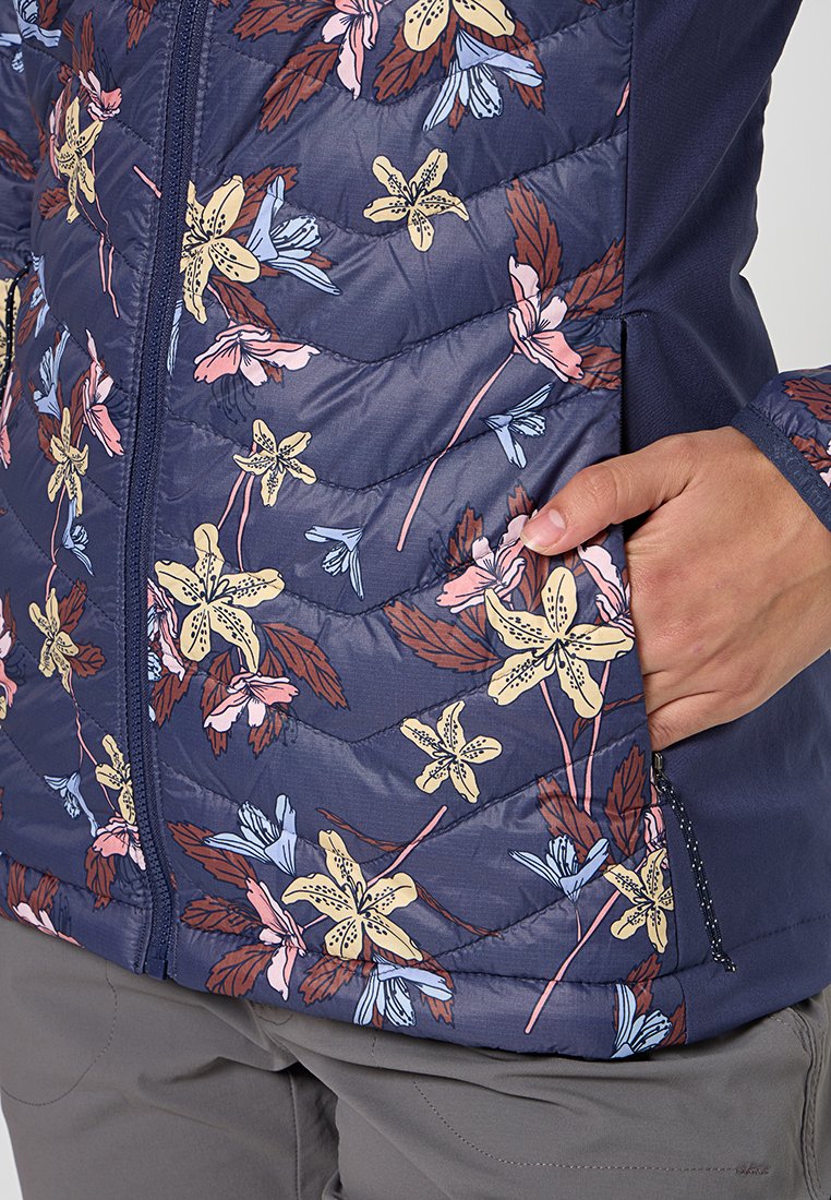 Chaqueta de cuadro azul marino con un patrón floral en rosa, amarillo y azul, con un bolsillo con cremallera y un diseño ajustado.